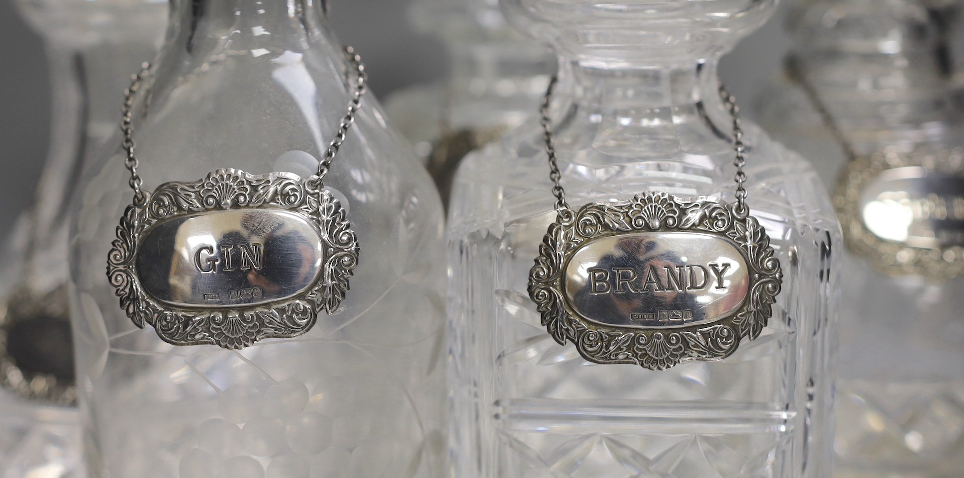 A silver plated oval tray, five assorted cut glass decanters and five assorted silver wine labels.